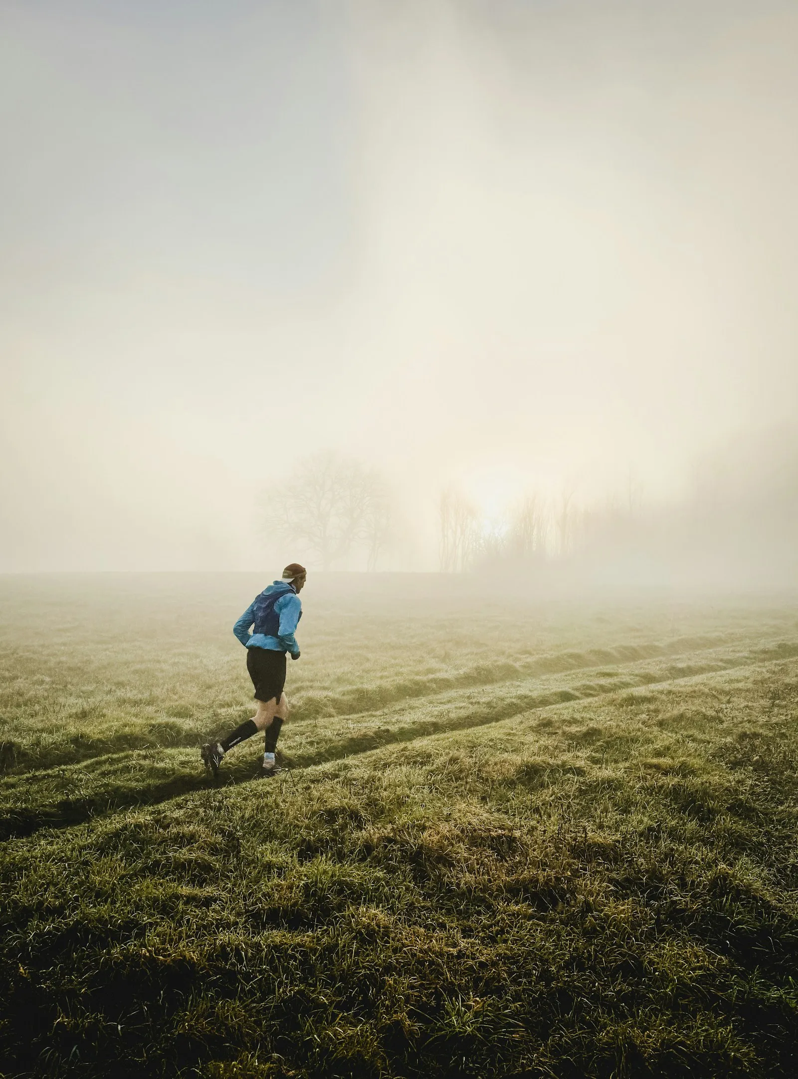 A runner on a trail in a misty field at sunrise.